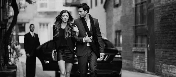 Man and woman walking away from limo with chauffeur.